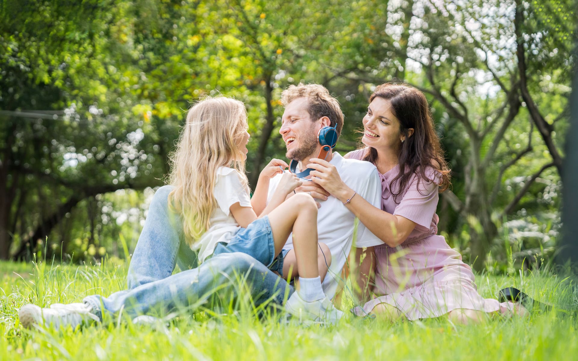 parents and child seated in a field and playing with over-ear headphones